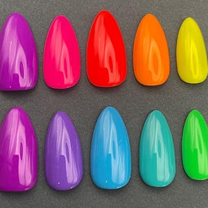 May include: A collection of ten glossy, almond-shaped artificial nails in a variety of vibrant colors. The colors include purple, hot pink, red, orange, yellow, blue, teal, and green. The nails are arranged in two rows of five.