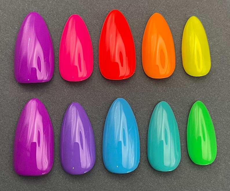May include: A collection of ten glossy, almond-shaped artificial nails in a variety of vibrant colors. The colors include purple, hot pink, red, orange, yellow, blue, teal, and green. The nails are arranged in two rows of five.
