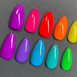 May include: A collection of ten brightly colored, almond-shaped artificial nails. The colors include shades of purple, pink, red, orange, yellow, blue, teal, and green. The nails are arranged on a gray surface, showcasing a vibrant spectrum of hues.