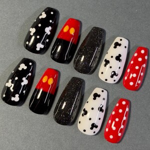 May include: A set of ten coffin-shaped false nails. Designs include black with white spots, red with yellow circles, black glitter, white with black Mickey Mouse shapes, and red with white polka dots.