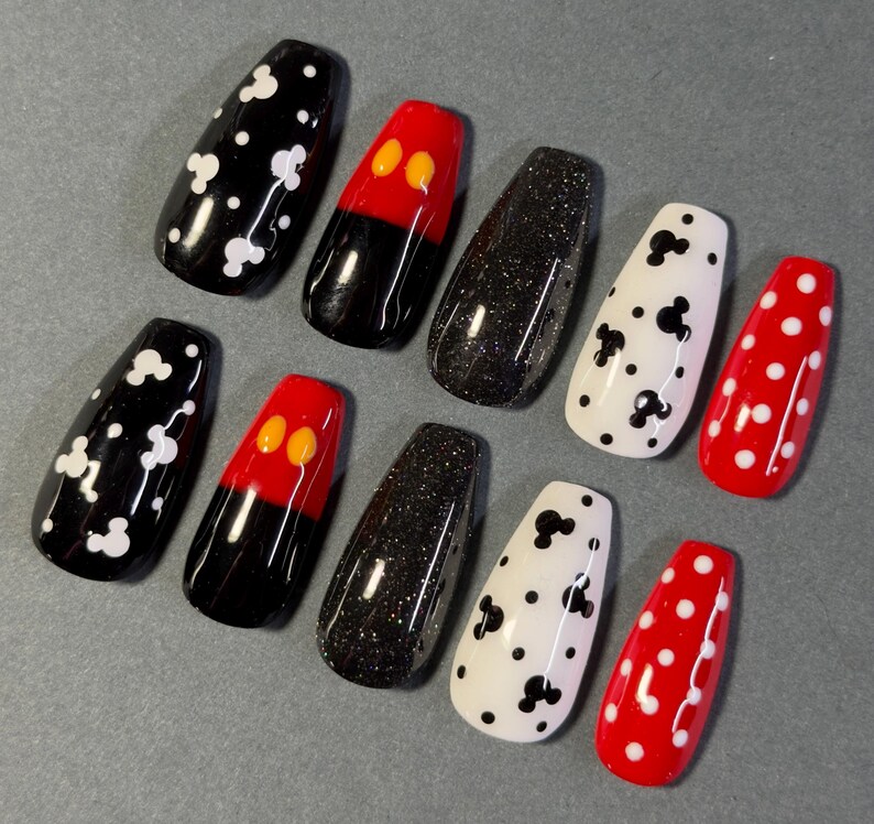 May include: A set of ten coffin-shaped false nails. Designs include black with white spots, red with yellow circles, black glitter, white with black Mickey Mouse shapes, and red with white polka dots.