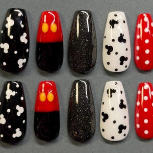 May include: Ten artificial nails in various designs. The designs include black with white polka dots, black with white Mickey Mouse shapes, black with red and yellow Mickey Mouse shapes, black glitter, white with black polka dots, and red with white polka dots.