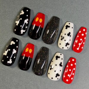 May include: A set of ten artificial nails in various designs. The nails feature black with white polka dots, red with black and yellow accents, black glitter, white with black Mickey Mouse shapes, and red with white polka dots.