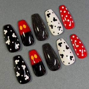 May include: A set of ten press-on nails in various designs. The nails feature black and white Mickey Mouse patterns, red and black Mickey Mouse designs, black glitter, and red nails with white polka dots. The nails are coffin-shaped.
