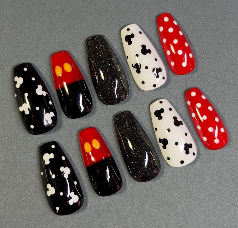 May include: A set of ten press-on nails in various designs. The nails feature black and white Mickey Mouse patterns, red and black Mickey Mouse designs, black glitter, and red nails with white polka dots. The nails are coffin-shaped.
