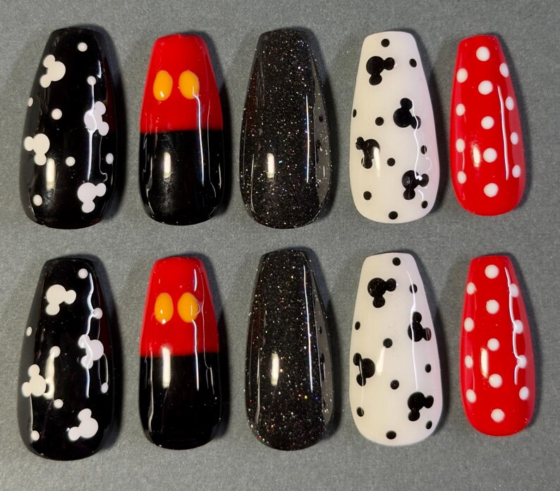 May include: Ten artificial nails in a variety of designs. The nails feature black with white Mickey Mouse shapes, red and black Mickey Mouse designs, black glitter, white with black Mickey Mouse shapes, and red with white polka dots.