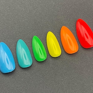 May include: A collection of ten glossy, almond-shaped artificial nails in a rainbow of colors. The colors include purple, blue, teal, green, yellow, orange, red, pink, and another shade of purple. The nails are arranged in a diagonal line.