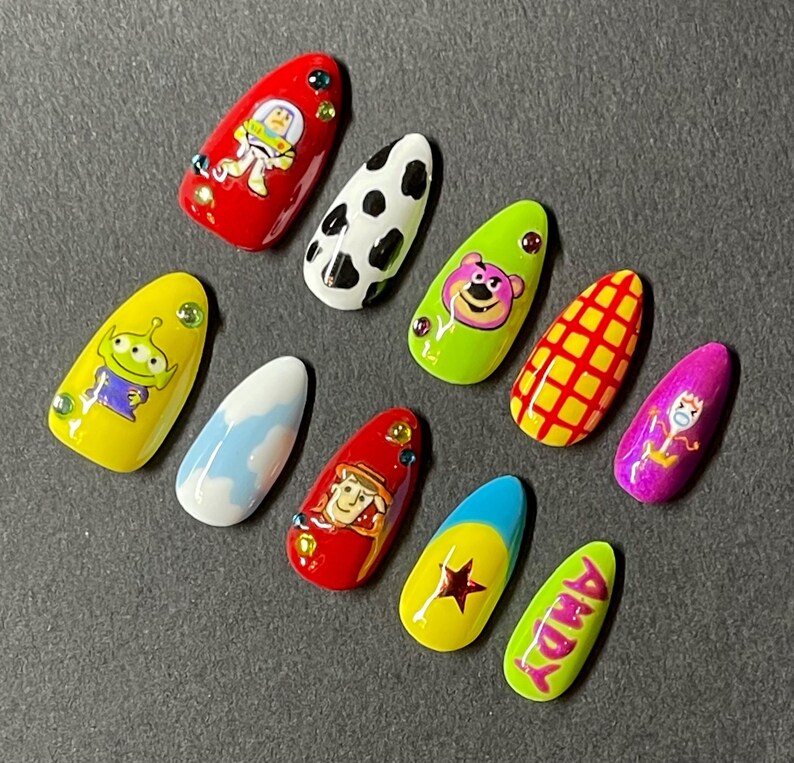 Op de afbeelding: Een set van tien kunstnagels, elk met een uniek ontwerp ge&iuml;nspireerd op de animatiefilm Toy Story. De nagels tonen personages als Buzz Lightyear en Woody, samen met andere thema-patronen en de naam "Andy".