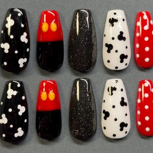 May include: A set of ten artificial nails in various designs. The designs include black with white Mickey Mouse shapes, red with yellow Mickey Mouse ears, black glitter, white with black Mickey Mouse shapes, and red with white polka dots.