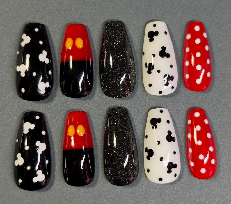 May include: A set of ten artificial nails in various designs. The designs include black nails with white Mickey Mouse shapes, red and black nails with yellow Mickey Mouse ears, black glitter nails, white nails with black Mickey Mouse shapes, and red nails with white polka dots.