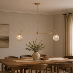 May include: A linear chandelier with a brass finish featuring two ribbed glass globe shades suspended from a central horizontal bar. The fixture is attached to the ceiling by a single vertical rod and includes thin support wires for stability.