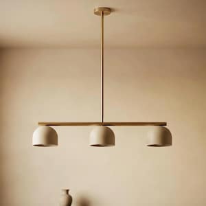May include: A linear pendant light fitting featuring a central brass-toned rod suspended from a matching circular ceiling canopy. Three matte beige dome-shaped shades are attached horizontally along the rod, providing downward-facing illumination.