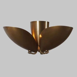 May include: A brass-colored ceiling light fixture with a central cylindrical element and three curved, petal-like shades. The fixture has a warm, metallic finish and is designed for overhead lighting.