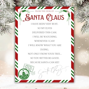 Peut inclure: Une lettre festive du Père Noël, avec une bordure à rayures rouges et blanches et des accents verts. Le texte indique "From the Desk of Santa Claus" et comprend un message sur la surveillance des enfants. Un timbre de la poste du Pôle Nord est également visible.