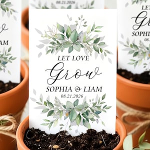 Puede incluir: Cuatro macetas de terracota llenas de tierra, cada una con una tarjeta blanca con el texto "LET LOVE Grow SOPHIA & LIAM 08.21.2026" y un diseño floral en acuarela. Las macetas están atadas con hilo.
