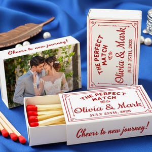 May include: White matchboxes with red accents and text. One box features a photo of a couple. The text on the boxes reads "The Perfect Match," names, and a date. The phrase "Cheers to new journey!" is also visible.