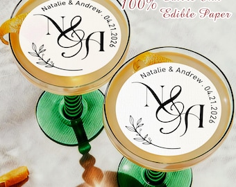 May include: Two cocktails in coupe glasses with green stems, each topped with a white edible paper disc. The discs feature the names "Natalie & Andrew" and the date "04.21.2026", with the text "100% Edible Ink Edible Paper".