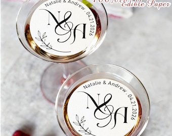 May include: Two martini glasses filled with a golden liquid, each with a white edible paper disc. The discs feature the names "Natalie & Andrew" and the date "04.21.2026" with a decorative flourish. Text reads "100% Edible Ink Edible Paper."