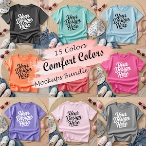 May include: A collection of t-shirts in various colors, including gray, teal, orange, pink, purple, and light pink. Each shirt features the text "Your Design Here" in a script font. The image also includes the text "15 Colors Comfort Colors Mockups Bundle."