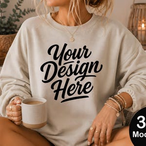 Può includere: Una felpa beige a girocollo con il testo nero Your Design Here stampato sul davanti. La felpa presenta maniche lunghe con polsini a coste e una vestibilità rilassata. Una tazza in ceramica è tenuta in una mano e diversi braccialetti di perline sono indossati al polso.
