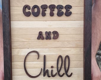 Puede incluir: Un letrero de pared rectangular de madera con un marco marrón oscuro y un fondo de listones horizontales de color beige claro. El letrero muestra el texto recortado en relieve de color marrón oscuro "COFFEE AND Chill" centrado en la parte frontal.