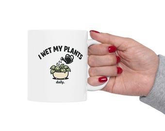 Puede incluir: Taza de cerámica blanca con el texto "I WET MY PLANTS" y un gráfico de una regadera vertiendo agua sobre una planta. La palabra "daily" está debajo del gráfico de la planta. La taza está sostenida por una mano con esmalte de uñas rojo.