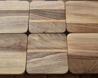 Puede incluir: Seis posavasos de madera con esquinas redondeadas están dispuestos sobre una superficie de madera. Los posavasos son de madera marrón clara y oscura, con vetas visibles. Los posavasos tienen forma cuadrada con esquinas redondeadas.