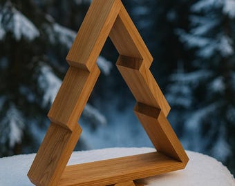 Puede incluir: Estantería triangular de madera en tono natural, que se asemeja a un árbol de Navidad estilizado. La estantería está construida con bloques de madera en capas, creando un diseño geométrico. Se encuentra sobre una superficie nevada con un fondo borroso de bosque.
