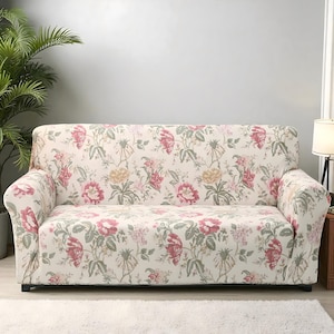 Puede incluir: Una funda de sofá con estampado floral en color crema. La funda presenta un patrón repetido de flores y hojas rosas, amarillas y verdes. La funda del sofá está diseñada para un sofá estándar de dos plazas.