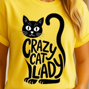 May include: Yellow t-shirt with a black cat design and the words "CRAZY CAT LADY" in a playful font. The cat's body forms the letters of the words. The shirt has short sleeves and a crew neck.