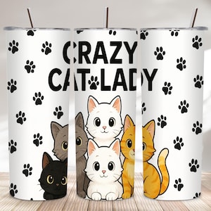 Könnte beinhalten: Ein weißer Becher mit dem Schriftzug "CRAZY CAT LADY" in Schwarz, verziert mit schwarzen Pfotenabdrücken. Das Design zeigt Cartoon-Katzen in Schwarz, Grau, Weiß und Orange. Der Becher hat einen Strohhalm.