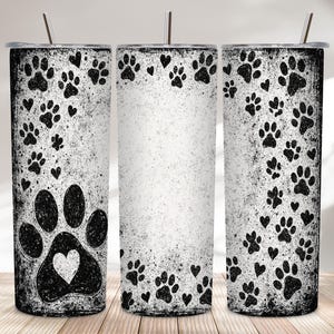 May include: Three stainless steel tumblers with black paw prints and hearts on a distressed white background. Each tumbler has a silver lid and a silver straw. The design includes a large paw print with a heart.