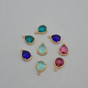 以下が含まれることがあります： ティアドロップ型のペンダントが8つ。色はティール、ブルー、ピンクなど。各ペンダントは、金色のねじれたロープのような縁取りと、チェーンや他のジュエリーコンポーネントに取り付けるための小さなループが付いています。