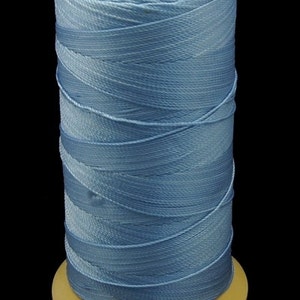 Puede incluir: Una bobina de hilo azul claro, bien enrollada alrededor de un núcleo de madera. El hilo tiene un brillo sutil, y la bobina se encuentra sobre un fondo negro, resaltando el color y la textura del hilo. Ideal para proyectos de costura y manualidades.