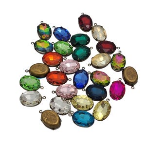 May include: A collection of oval-shaped, colorful gemstone pendants with small loops for attaching to jewelry. The gemstones are in various colors, including blue, green, pink, and iridescent, with a metallic bronze-colored setting.