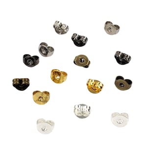 May include: A collection of earring backs in various metallic finishes, including silver, gold, and black. The earring backs are in different shapes and sizes, designed to secure earrings. The image shows a variety of styles, suitable for different earring types.