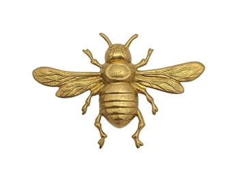 May include: A gold-coloured bee-shaped decorative object with outstretched wings. The bee has detailed wings, legs, and antennae. The object is likely made of metal and is designed to be a decorative accent.