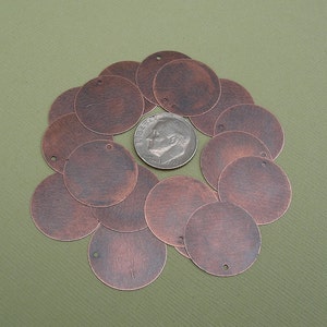 May include: A group of 12 copper-colored metal circles with a hole in the center. The circles are arranged in a circle around a dime.