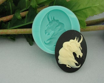 May include: A silicone mould and a finished cameo of a white unicorn head, both in an oval shape. The mould is turquoise blue and the cameo is black with a white unicorn head.