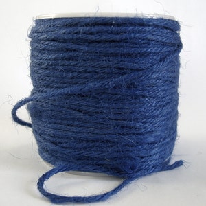 May include: A spool of blue twine, a type of string made from natural fibers, is wound tightly around a cardboard tube. The twine is a deep, rich blue color and has a slightly rough texture.
