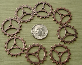 May include: Eight copper-colored gear charms with a three-spoke design. The gears are arranged in a circle around a US dime.