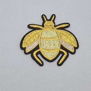 May include: A gold embroidered bee patch with black outline and pink accents on the wings.