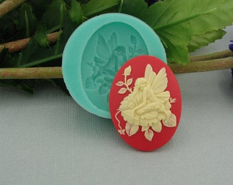 May include: A silicone mold for making a cameo of a fairy sitting on a flower. The mold is turquoise and the cameo is red with a white fairy.