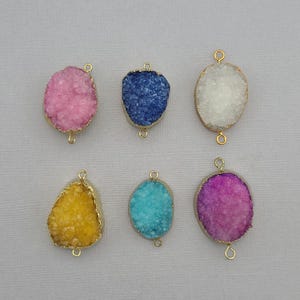 May include: Six colorful druzy pendants with gold-colored edges and loops. The pendants are in shades of pink, blue, white, yellow, turquoise, and purple. These pendants are ideal for jewelry making.