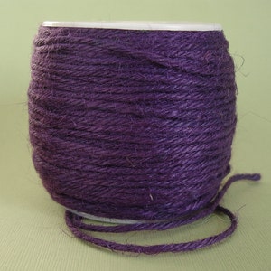 May include: A spool of purple twine wrapped around a white cardboard tube. The twine is made of natural fibers and has a rustic look.
