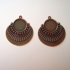 May include: Two copper-toned metal earring blanks with a circular cutout in the center and a decorative design around the edge.