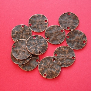 May include: A collection of ten round, copper-colored metal charms with a hammered texture. Each charm has two holes for attaching to jewelry or other crafts.