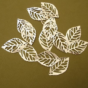 May include: A collection of ten silver metal leaves with a delicate, intricate cut-out design. The leaves are arranged in a cluster, with some overlapping.