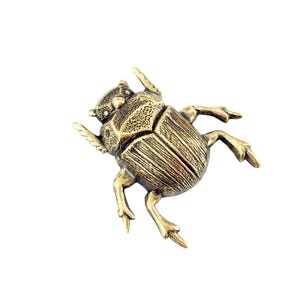 May include: A detailed, bronze-colored scarab beetle figurine. The beetle has textured wings and legs, and is set against a white background. The figurine is a decorative item, possibly for display or as a collectible.