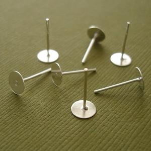 May include: Six silver earring posts with flat round backs. The posts are approximately 2.5 cm long and the backs are about 1.25 cm in diameter.